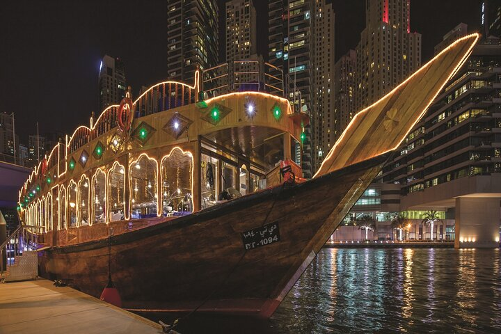 Experience the charm of Dubai Marina on a traditional dhow savoring gourmet cuisine while taking in stunning views of modern skyscrapers illuminated against the night sky.